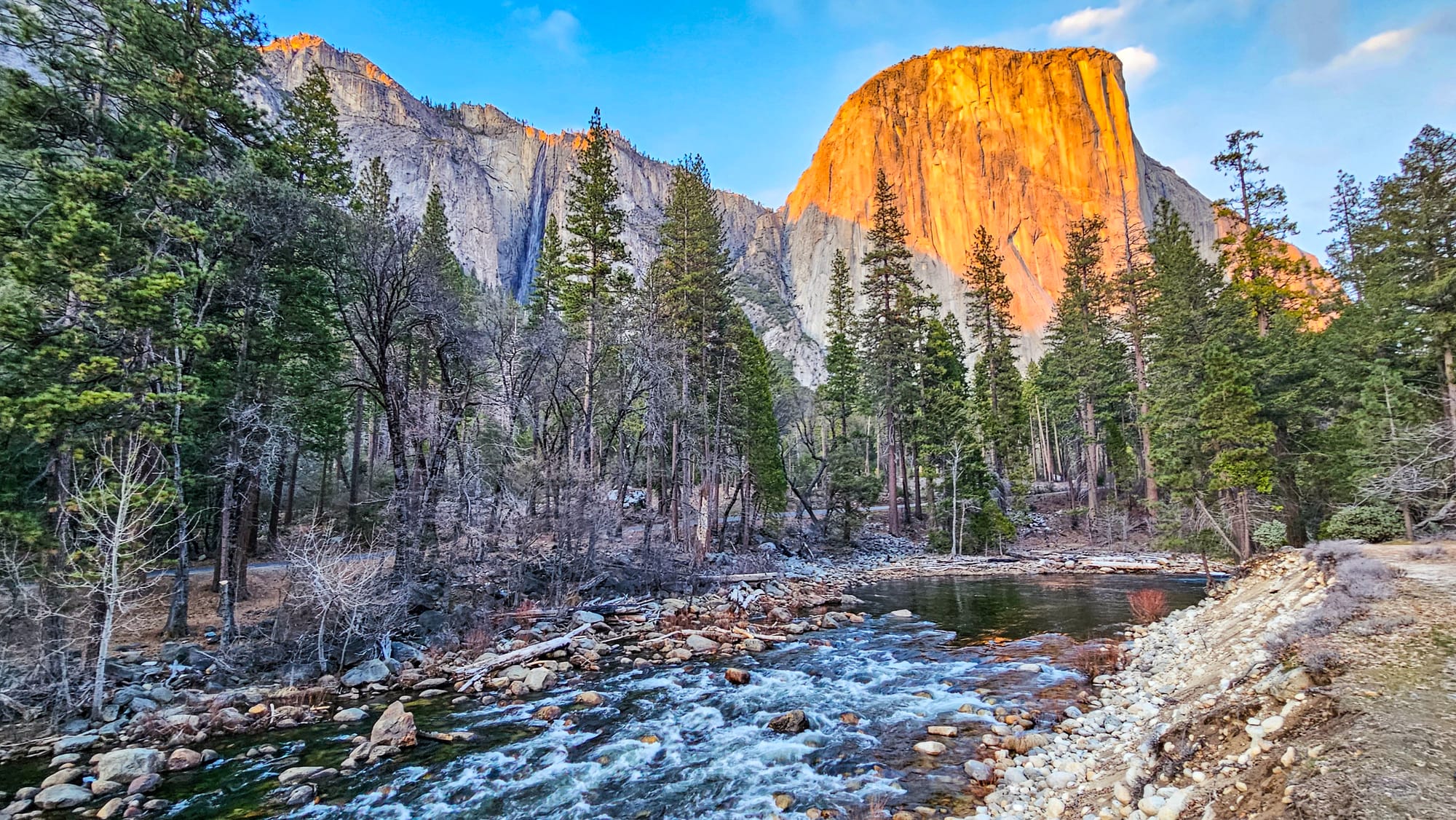 Ribbon Fall (waterfall), El Capitan glowing orange and the Merced River lined with pine trees.