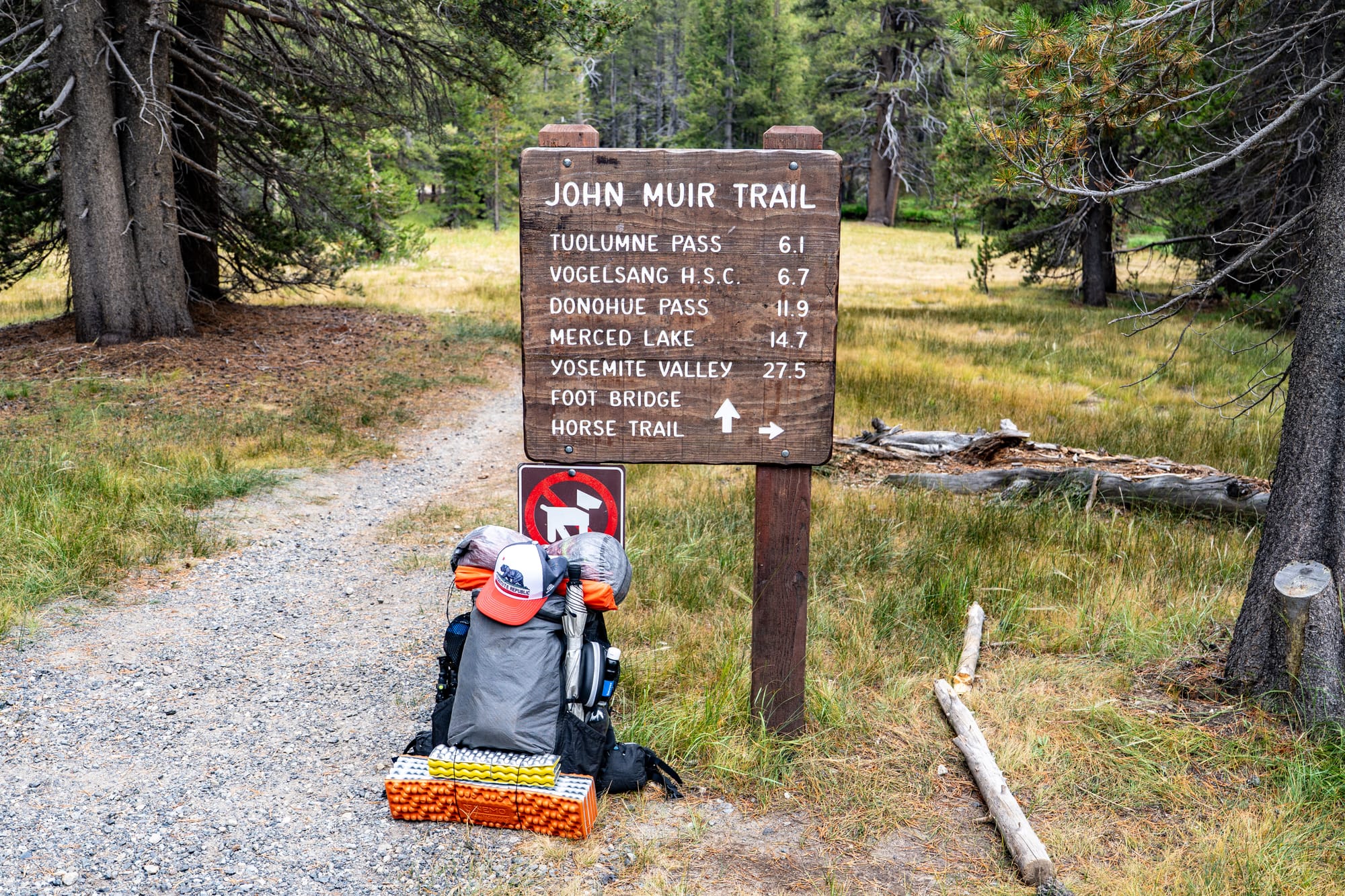 Yosemite.Life backpack leaned up against a trail sign in Tuolumne Meadows. Sign says John Muir Trail and other Yosemite backcountry destinations.