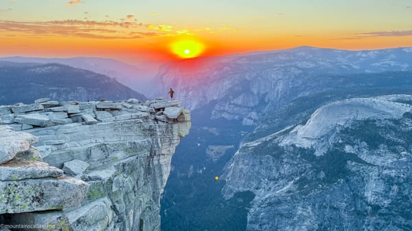 Hiker standing on The Visor of Half Dome with an orange and red sunset over Yosemite Valley | Yosemite Life